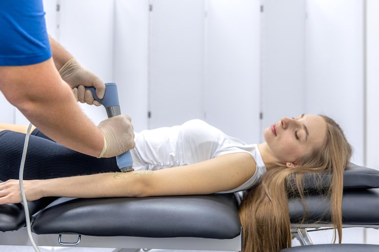 Photograph of a patient comfortably lying on a treatment table with Emsculpt Neo paddles strapped to the abdomen and arms — relaxed expression, soft natural lighting, sage and cream decor