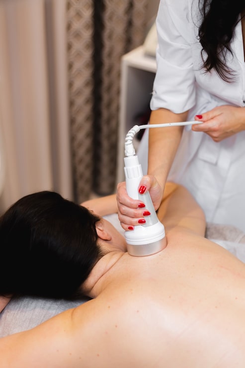 Professional photograph of an Emsculpt Neo body sculpting device with treatment paddles positioned on a patient's abdomen — modern aesthetic equipment in a clean, well-lit treatment room with sage and warm cream tones