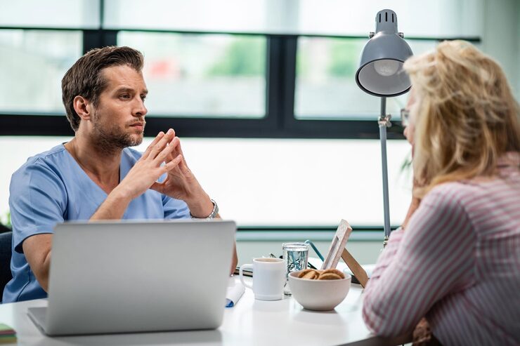 Photograph of an EVOX emotional reframing session — patient speaking into a microphone with practitioner observing voice-pattern feedback on a screen in a serene office
