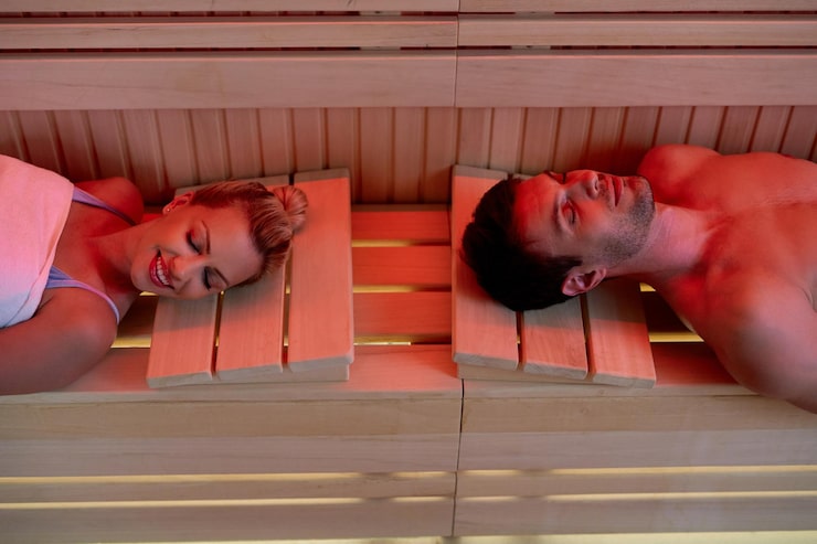 Photograph of a patient relaxing on a Migun thermal massage bed with infrared rollers along the spine — warm ambiance with sage and cream linens, calm spa-like atmosphere
